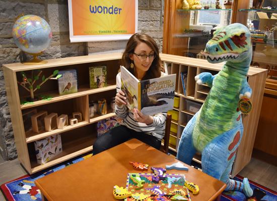 Lady reading in childrens play area to a toy dinosaur